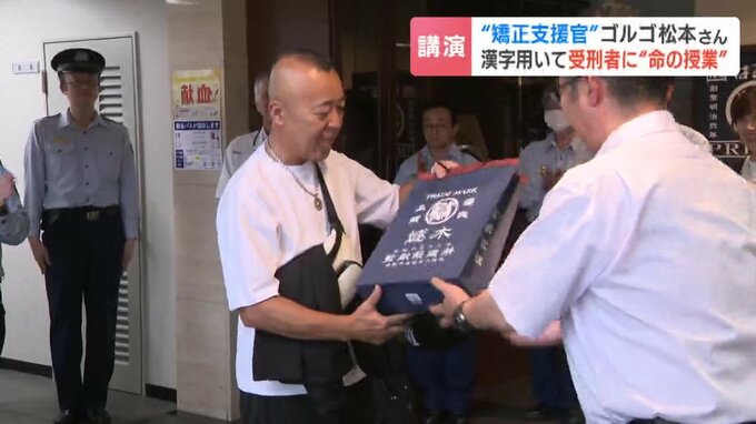 記念品として贈られた受刑者手作りの手提げ袋を受け取るゴルゴ松本さん